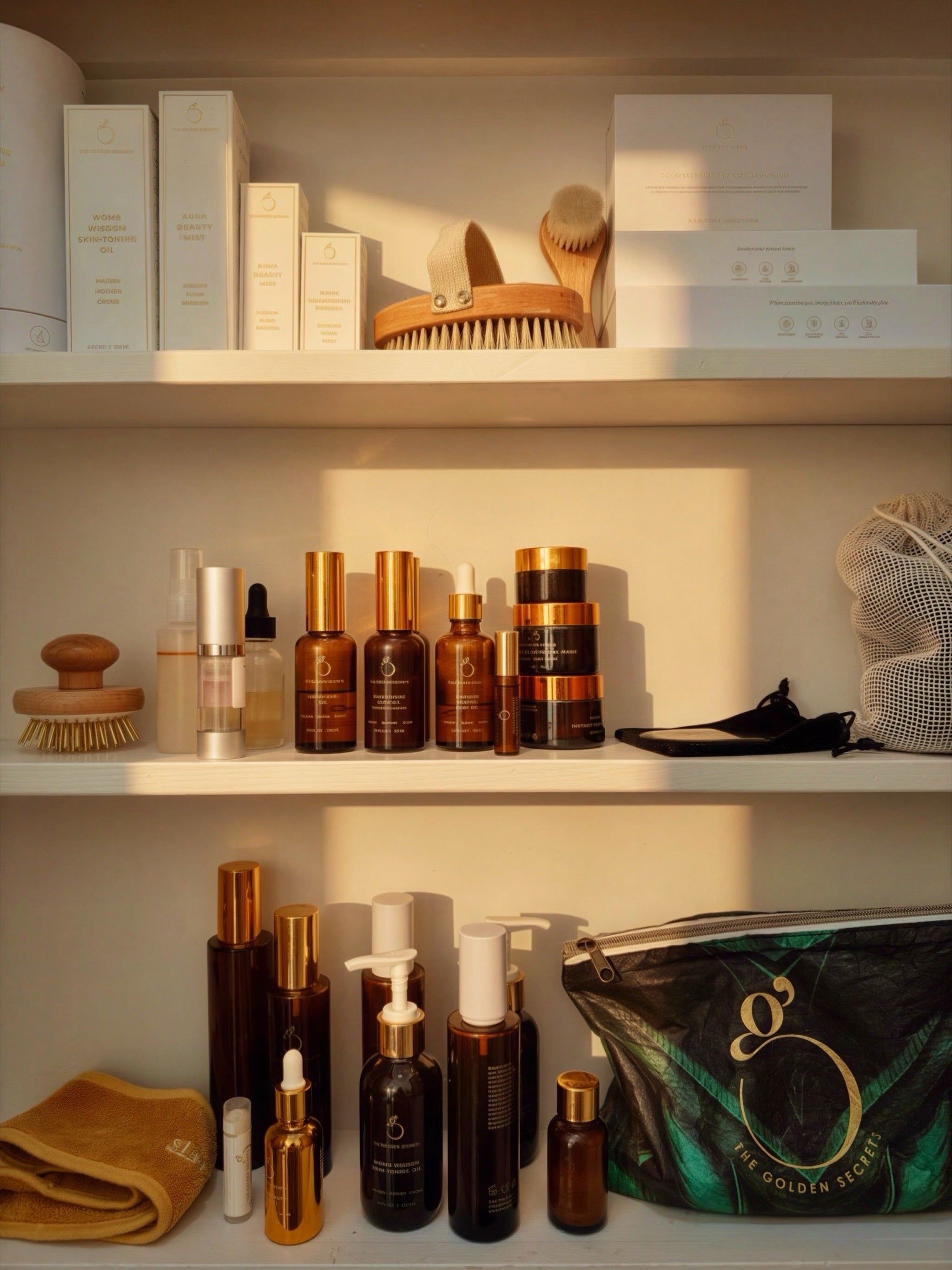 Shelves with neatly arranged skincare products in brown and gold bottles, brushes, boxes, a mesh bag, and a branded pouch, all bathed in warm sunlight.