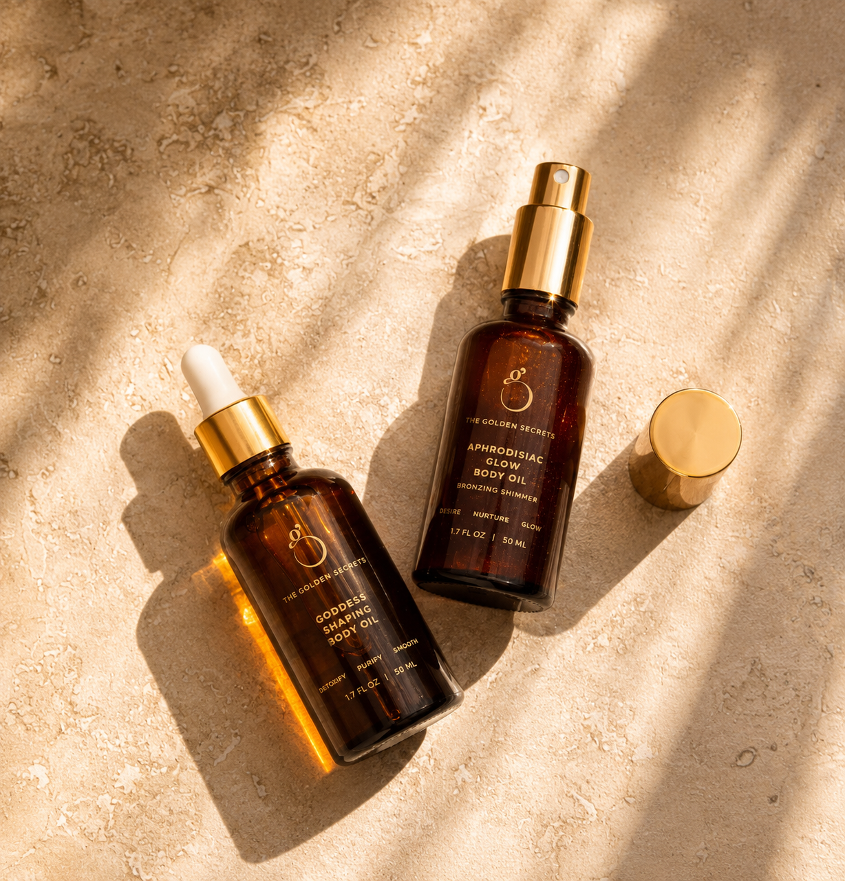 Two amber glass bottles with gold caps, labeled as part of the Sculpt & Glow Duo by THE GOLDEN SECRETS, rest on a textured beige surface bathed in soft sunlight and gentle shadows. These luxurious glow body oils are specially formulated to nourish your skin, enhance its natural radiance, and help diminish the appearance of stretch marks—leaving you luminous all day long.