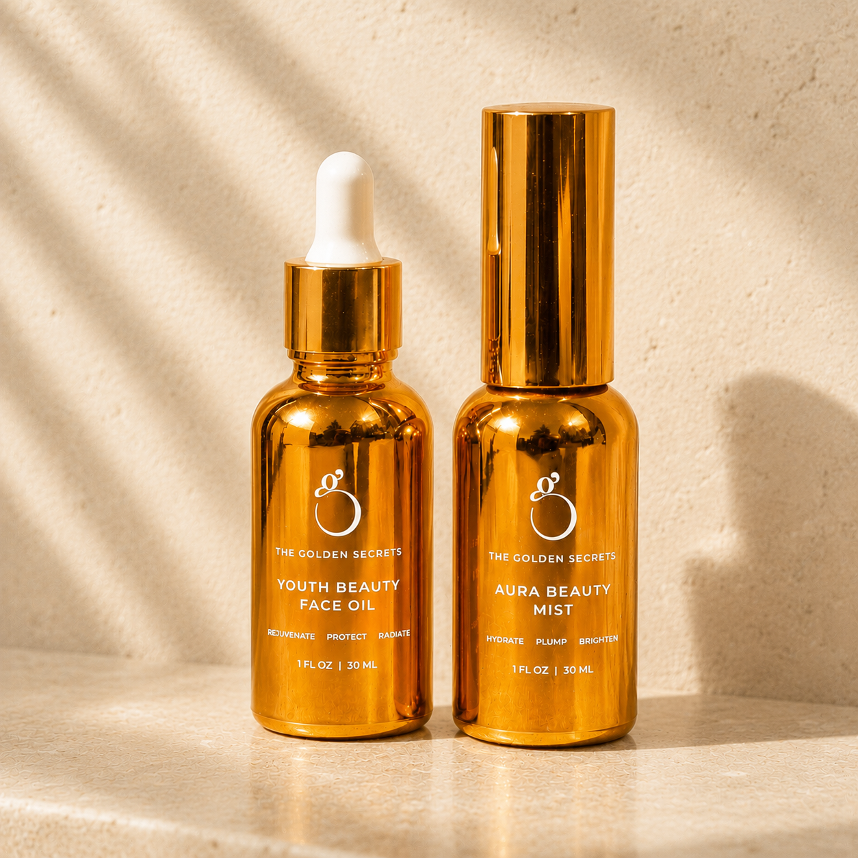 Two gold bottles of the Dynamic Duo by THE GOLDEN SECRETS, one with a dropper labeled Youth Beauty Face Oil and one with a spray nozzle labeled Aura Beauty Hydrating Mist, are displayed on a beige surface in sunlight.