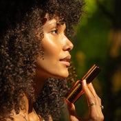 Woman applying lipstick with a blurred natural background