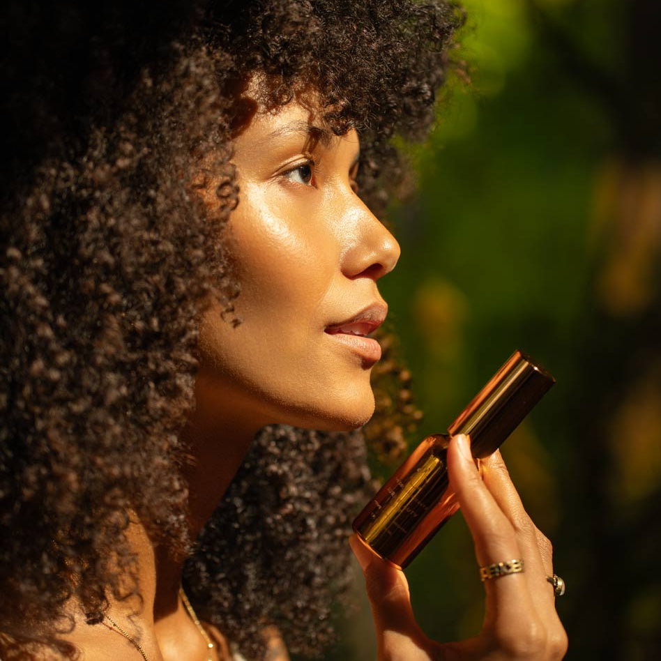 Woman applying lipstick with a blurred natural background
