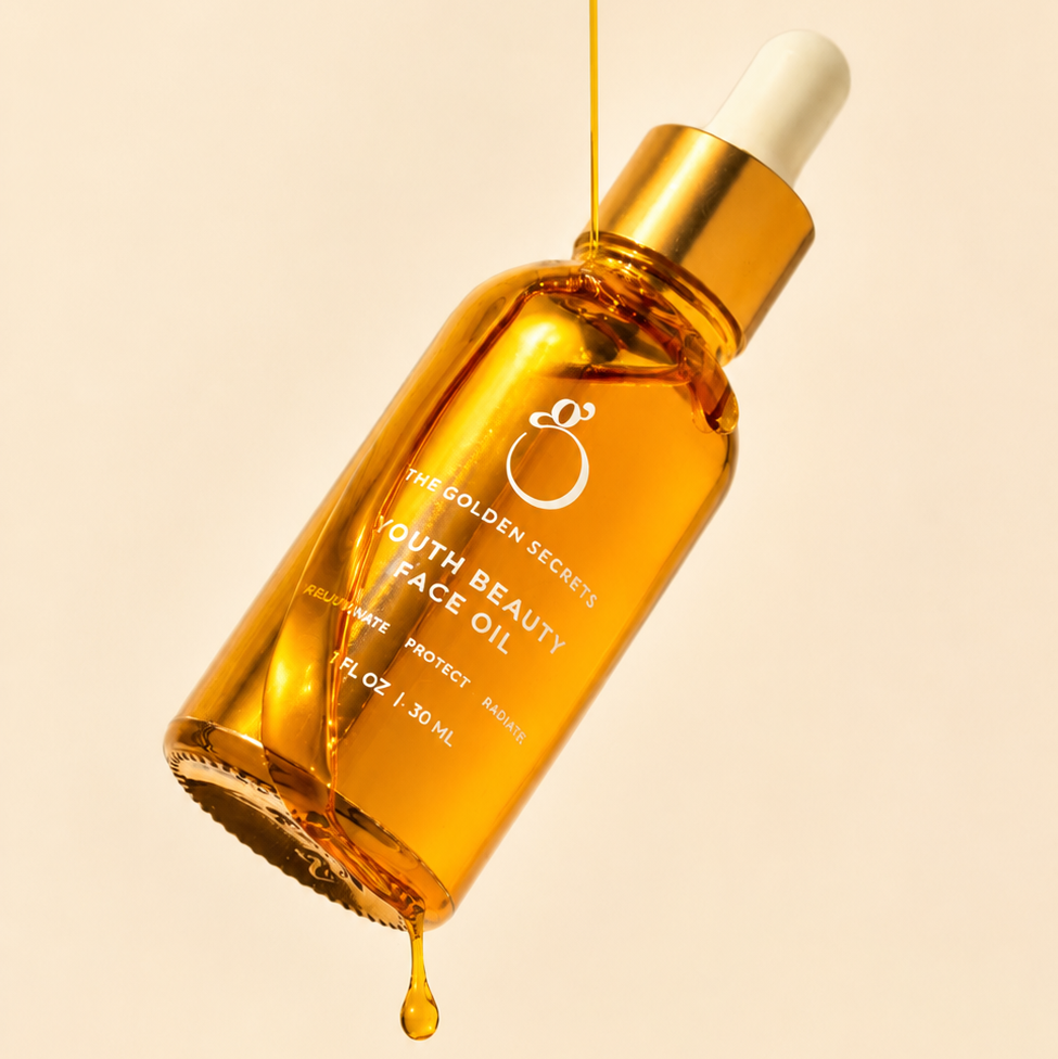 An amber glass dropper bottle of THE GOLDEN SECRETS Youth Beauty Face Oil, adorned with a gold cap, is artfully tilted as luminous, anti-aging oil glistens on the dropper and bottle against a soft beige background, capturing the allure of radiant skin.
