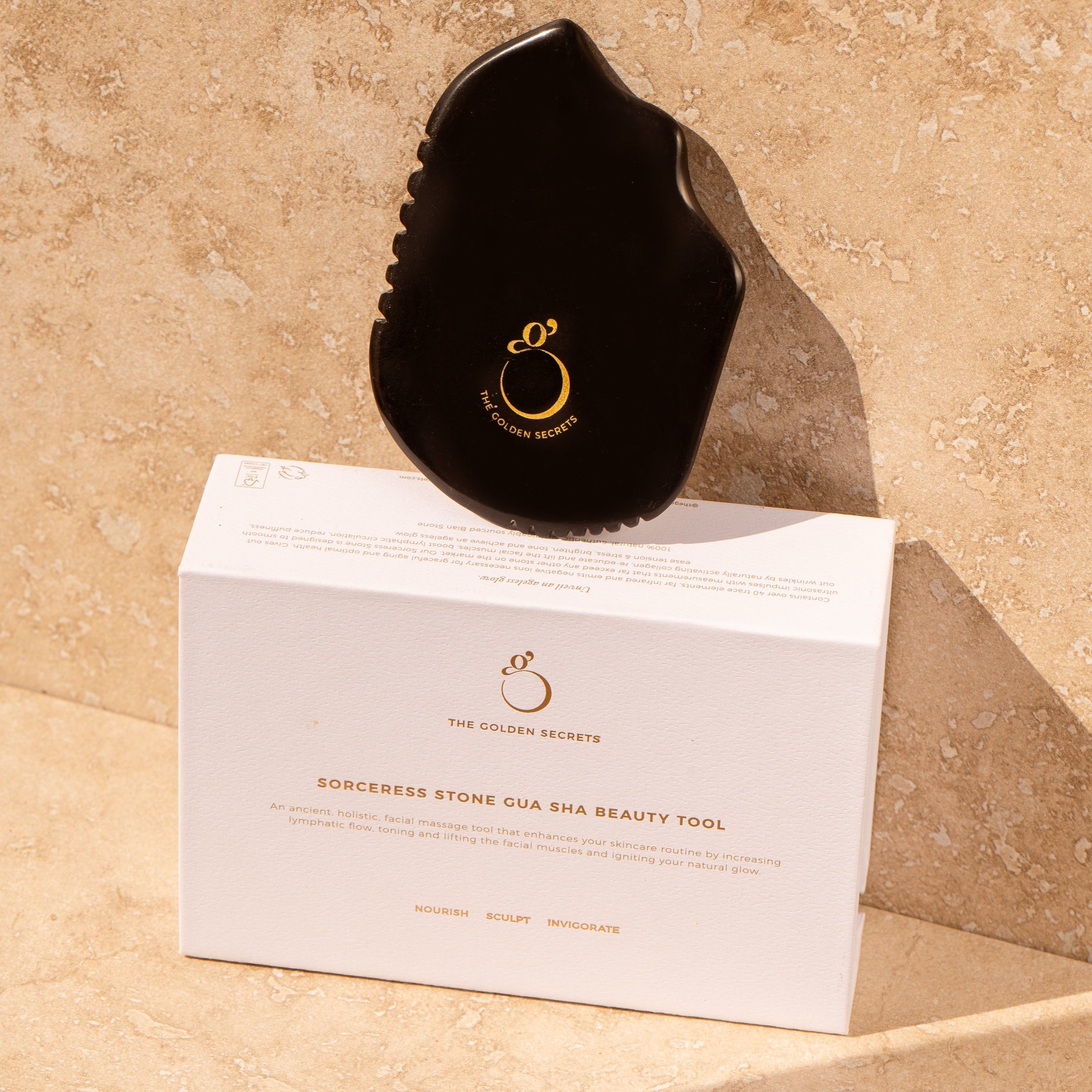 Black, heart-shaped Sorceress Stone Gua Sha Beauty Tool resting on its white product box.