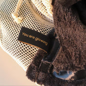A close-up of THE GOLDEN SECRETS Glowing Facial Cloths in a mesh drawstring bag alongside a black fabric item featuring a "You are glowing" gold label, showcasing their ultra-soft texture—perfect for makeup removal or use as facial cloths.