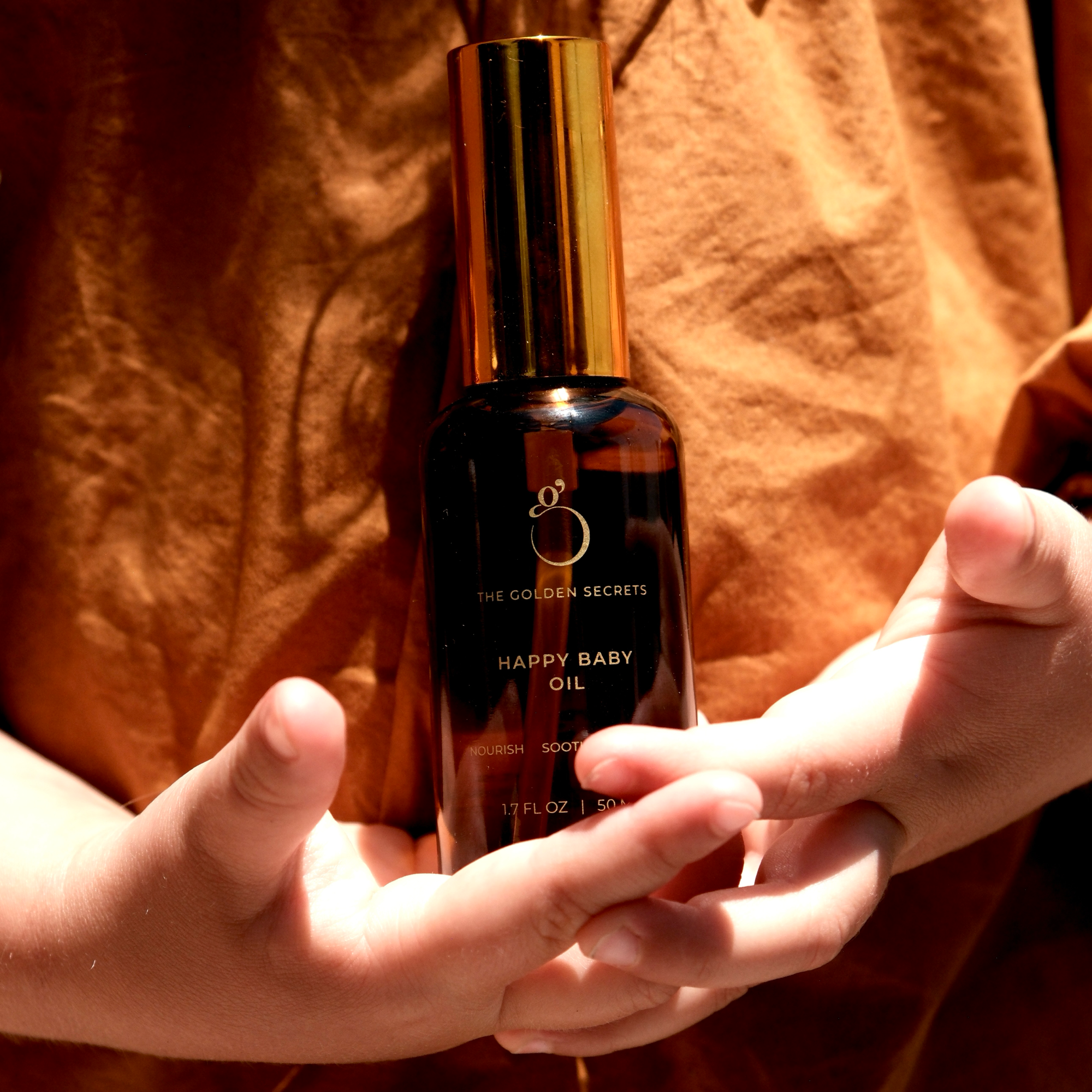 Person holding a bottle of Happy Baby oil with a warm, brownish tint.