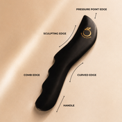The Sculpting Stone Gua Sha Body Tool by THE GOLDEN SECRETS features a sleek black design with labeled elements: pressure point edge, sculpting edge, comb edge, curved edge, and ergonomic handle. Crafted for lymphatic drainage and body sculpting, this elegant stone is displayed on a beige background and adorned with a gold logo near the top.