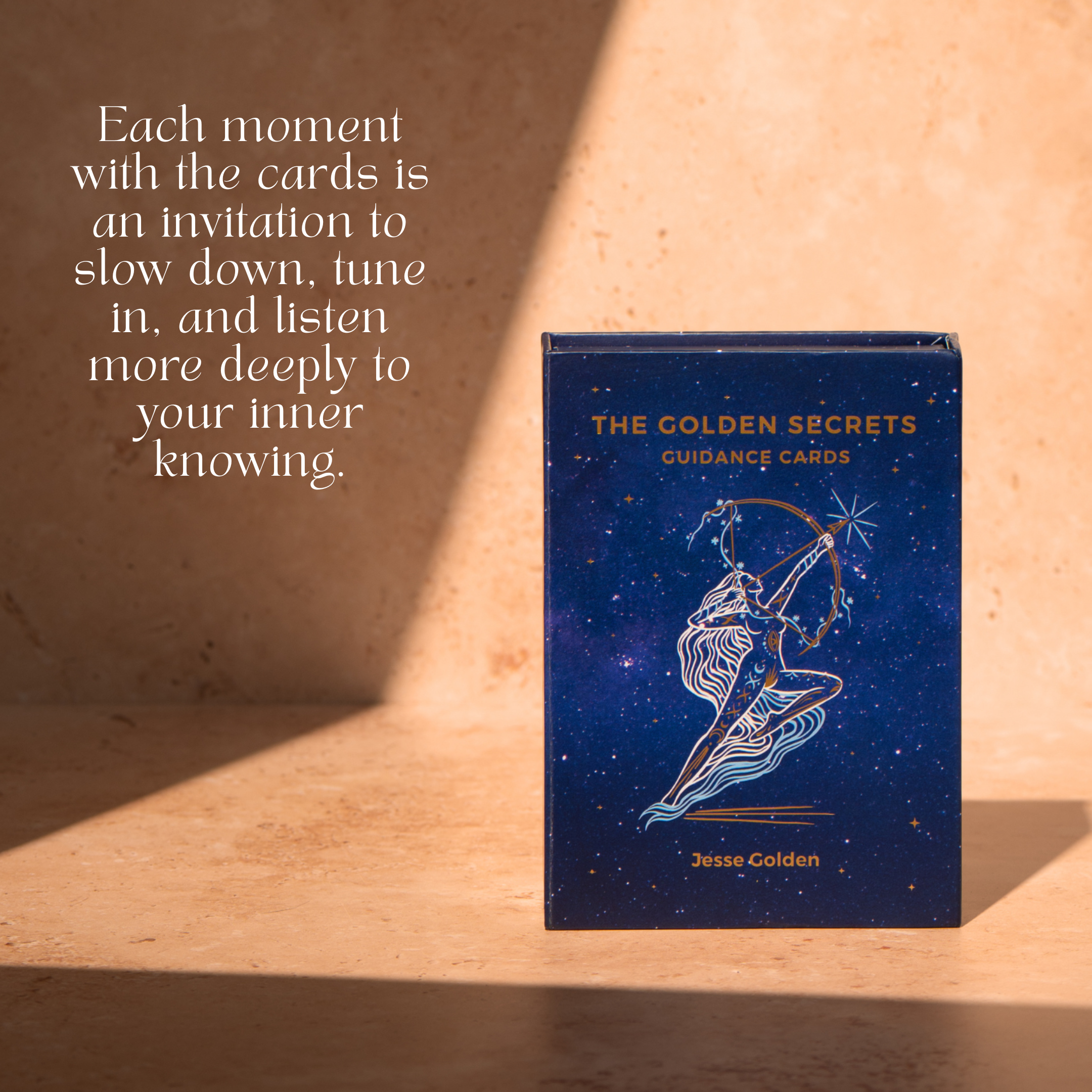 A box of THE GOLDEN SECRETS The Golden Secrets Guidance Cards rests on a sunlit surface. Next to it, text reads: “Each moment with The Golden Secrets Guidance Cards by THE GOLDEN SECRETS is an invitation to slow down, tune in, and listen more deeply to your inner knowing—offering comfort and peace along the way.”.