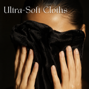 A person covers their face with a plush, black Glowing Facial Cloth from THE GOLDEN SECRETS. White text in the upper left reads “Ultra-Soft Cloths.” The lighting accentuates the cloth’s smooth texture and the person’s well-groomed hands, suggesting gentle cleansing ideal for makeup removal.