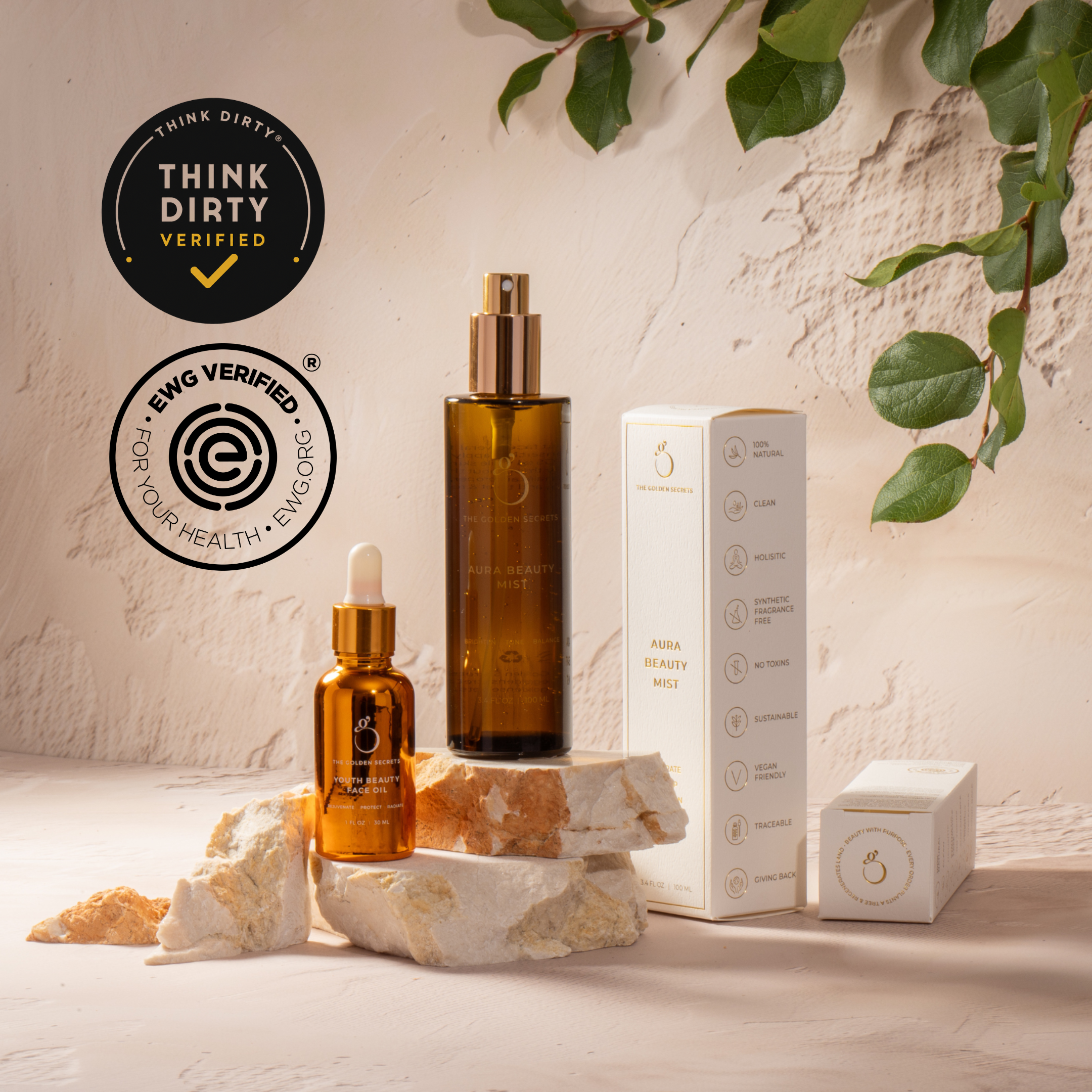 The Ultimate Glow Trio Kit by THE GOLDEN SECRETS features brown glass skincare bottles and a white box arranged on rock pieces, promising to hydrate, nourish, and lift your skin. Green leaves hang in the top right corner, while “Think Dirty Verified” and “EWG Verified” badges are displayed on the left side of the image.