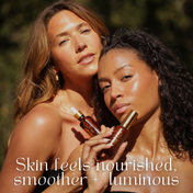 Two women with glowing skin pose outdoors, each holding a bottle of THE GOLDEN SECRETS Sculpt & Glow Duo. Sunlight highlights their smooth, radiant complexions. Text reads: “Skin feels nourished, smoother + luminous.”.