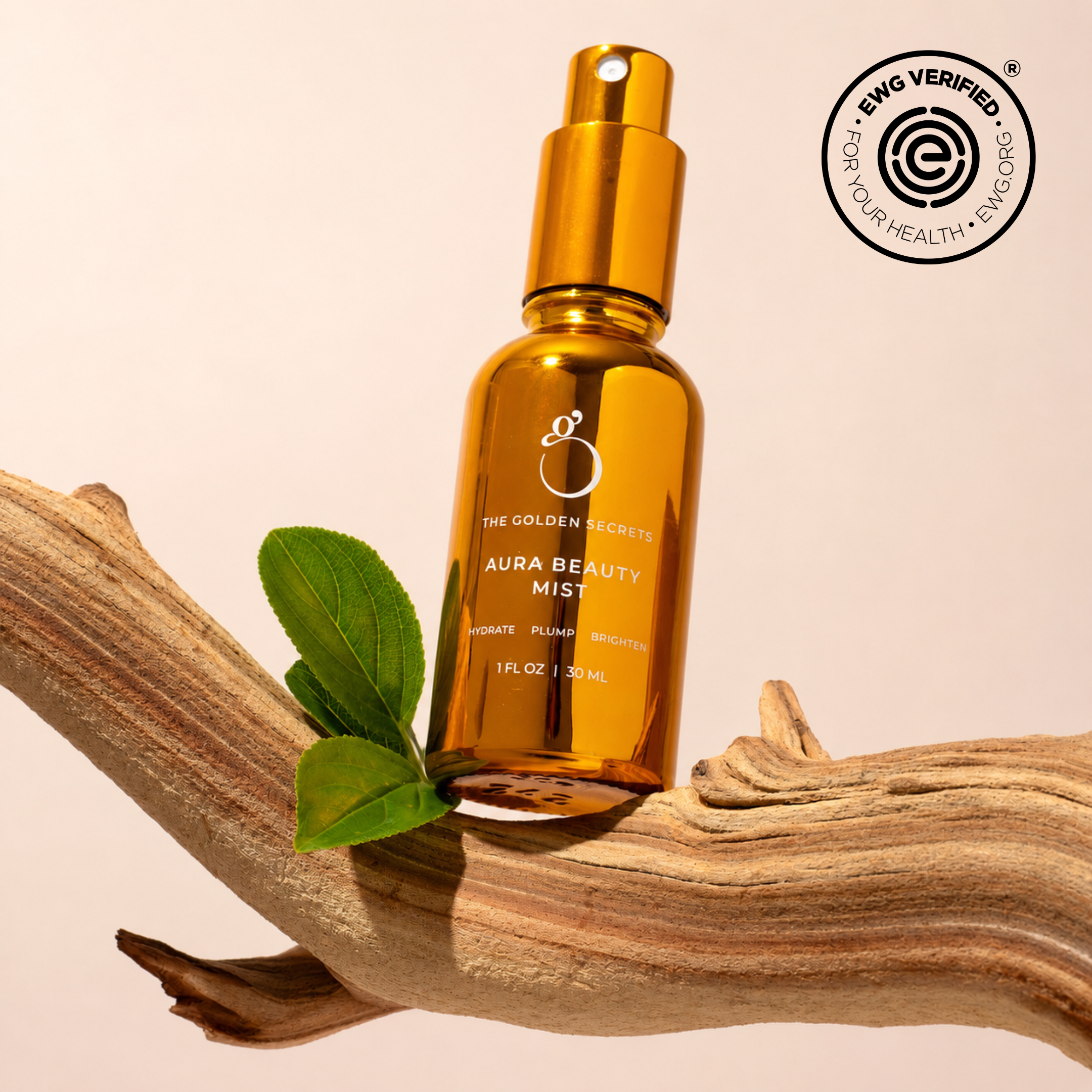 A golden Dynamic Duo bottle from THE GOLDEN SECRETS—perfect as a hydrating mist in your skincare routine— rests on a piece of wood with a green leaf, set against a beige background. The EWG Verified logo appears in the top right corner.